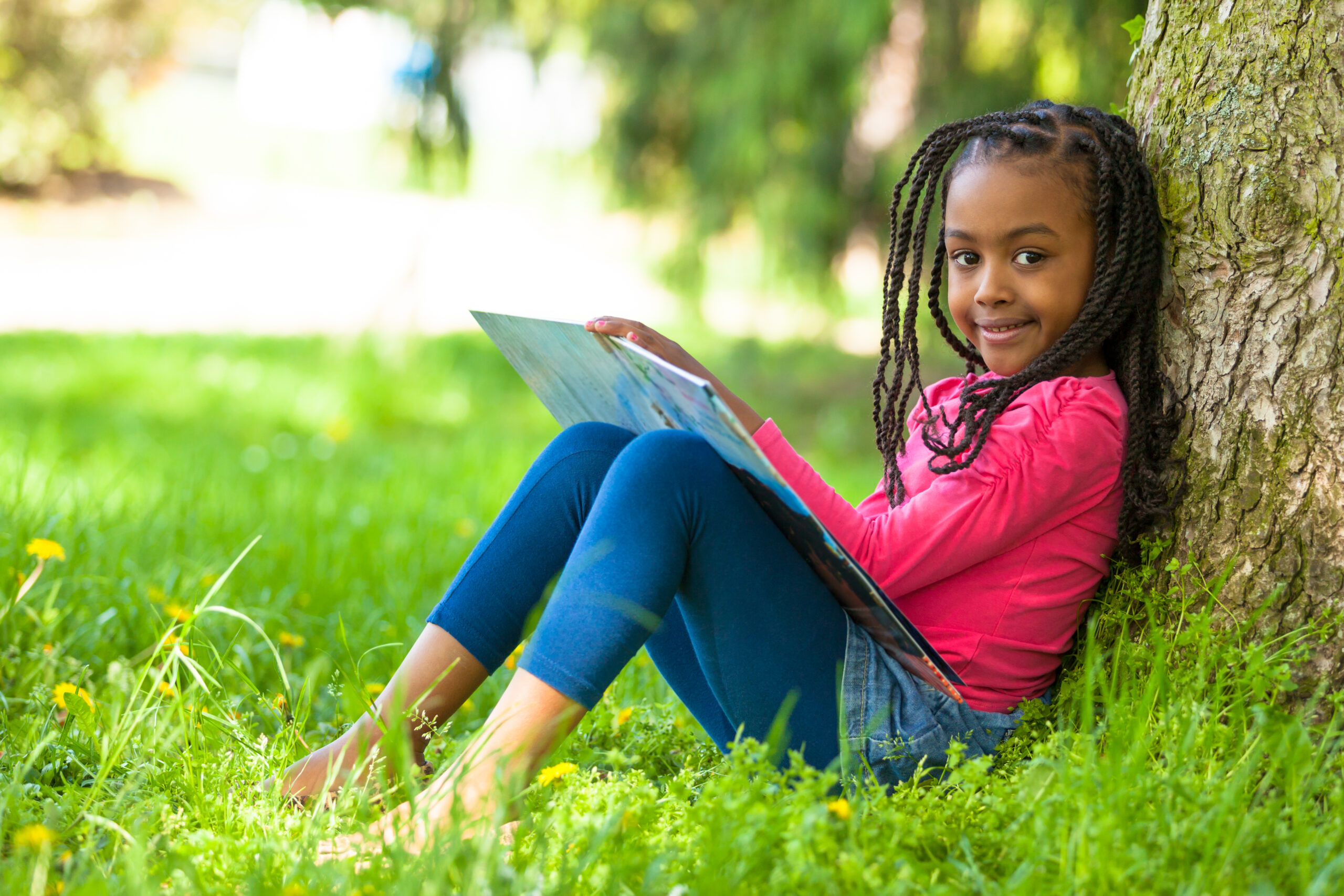 Outdoor portrait of a cute young black little girl reading a boo